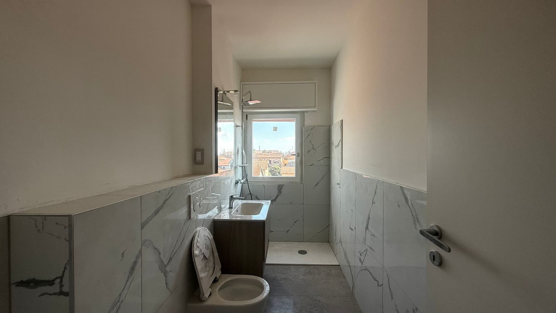 Marmo a mezza altezza e mobile scuro: Rivestimento a mezza altezza in effetto marmo, mobile scuro sospeso e doccia a filo pavimento.