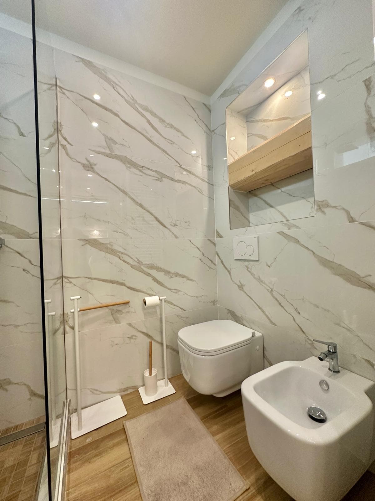 Calacatta oro e dettagli in ottone: Grandi lastre effetto calacatta con venature dorate, fondo doccia effetto legno e finiture in ottone.