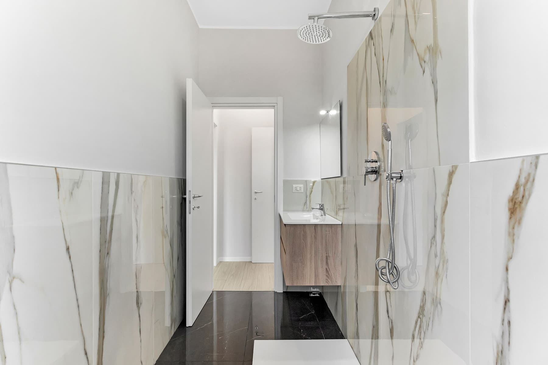 Marmo chiaro e pavimento scuro: Contrasto tra rivestimento chiaro effetto marmo e pavimento scuro, con doccia walk-in.