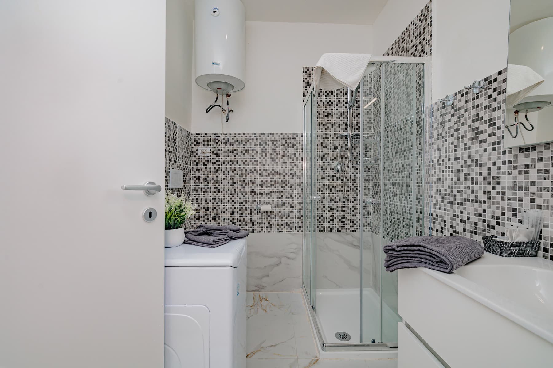 Mosaico e angolo lavanderia: Bagno con fascia a mosaico, box doccia angolare e vano lavatrice integrato.