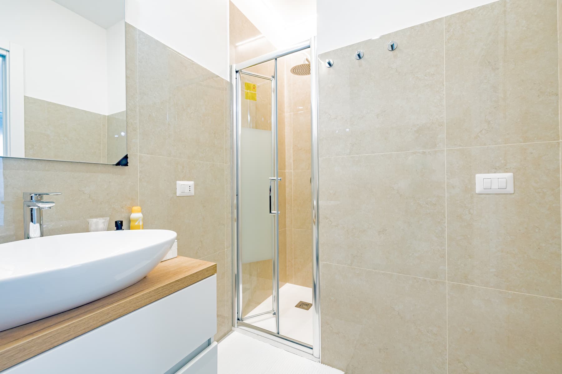 Travertino chiaro con angolo lavanderia: Rivestimento effetto travertino, lavabo d'appoggio su piano in legno e zona lavanderia dedicata.